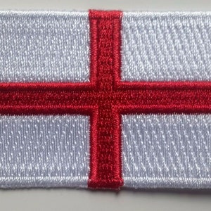 May include: Embroidered patch featuring the flag of England. The rectangular patch has a white background with a red cross of Saint George. The edges are neatly stitched with a white border. Ideal for jackets, bags, or other fabric items.