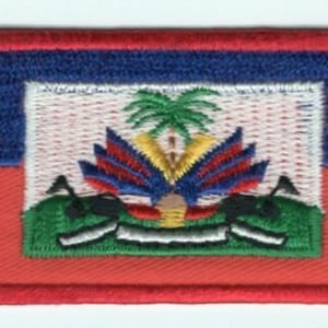 May include: An embroidered patch featuring the flag of Haiti. The flag is red, blue, and green with a coat of arms in the center. The coat of arms features a palm tree, a mountain, and a cannon.