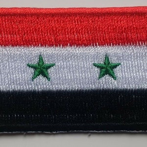 May include: Embroidered patch depicting the flag of Syria. The rectangular patch has horizontal stripes of red, white, and black. Two green, five-pointed stars are centered in the white stripe. The patch has a red border.