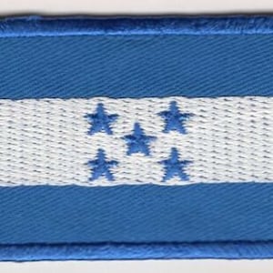 May include: A blue and white embroidered patch featuring the flag of Honduras. The flag has a white horizontal stripe with five blue five-pointed stars in the center, and two blue stripes above and below the white stripe.
