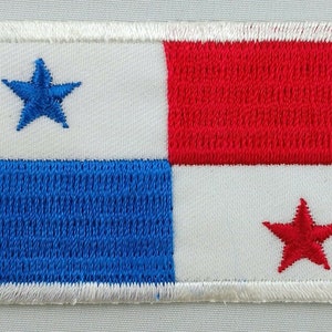 May include: An embroidered patch of the Panamanian flag. The flag is white with a blue stripe at the bottom and a red stripe at the top. There are three stars on the flag: one blue star in the top left corner and two red stars in the bottom right corner.