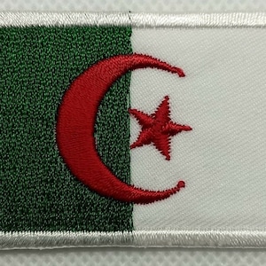 May include: A green, white, and red embroidered patch featuring the flag of Algeria. The flag has a white crescent moon and a five-pointed white star on a red background.
