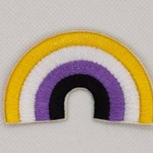May include: An embroidered patch in the shape of a rainbow arch. The patch features yellow, white, purple, black, and purple stripes.