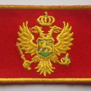 Peut inclure: Un écusson brodé rouge avec un aigle bicéphale doré et une couronne. L'aigle tient un bouclier avec un motif vert et bleu.