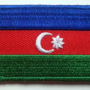 May include: An embroidered patch featuring the flag of Azerbaijan. The flag is a horizontal triband of blue, red, and green with a white crescent moon and star in the center of the red stripe.