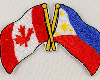 Peut inclure: Deux drapeaux brodés, l'un canadien et l'autre philippin, sont croisés l'un sur l'autre. Le drapeau canadien est rouge et blanc avec une feuille d'érable rouge. Le drapeau philippin est rouge, blanc et bleu avec un soleil jaune et trois étoiles.