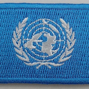 May include: A blue embroidered patch with the United Nations logo in white. The logo features a world map surrounded by olive branches.