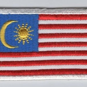 May include: A white embroidered patch with the flag of Malaysia. The flag features a blue field with a yellow crescent moon and a 14-pointed star, and 14 alternating red and white stripes.