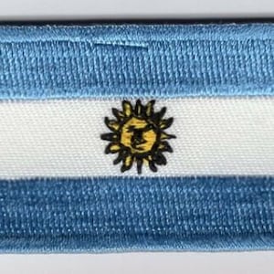 May include: A blue and white embroidered patch with a yellow sun in the center. The sun has a stylized face and rays.
