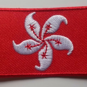 May include: A red embroidered patch with a white stylized flower design. The flower has five petals and a red center.