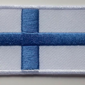 May include: A white fabric patch with a blue cross and a blue horizontal stripe in the centre. The patch is surrounded by a white border.
