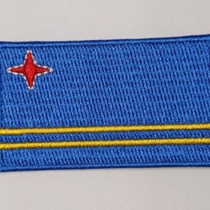 May include: A blue embroidered patch featuring a red star and two yellow stripes. The patch is a representation of the flag of Aruba.