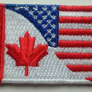 May include: A red, white, and blue embroidered patch featuring the Canadian flag on the left and the American flag on the right.