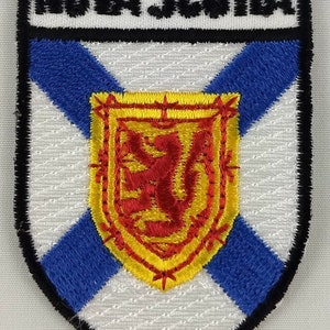 Peut inclure: Écusson brodé représentant le drapeau de la Nouvelle-Écosse. L'écusson est blanc avec une croix bleue et un lion rouge sur un écu jaune au centre. Les mots "NOVA SCOTIA" sont brodés en noir en haut.