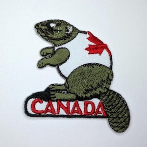 Peut inclure: Un écusson brodé représentant un castor vert portant un t-shirt blanc avec une feuille d'érable rouge. Le castor est placé au-dessus d'une bannière rectangulaire blanche à bordure noire portant le texte brodé en rouge CANADA.
