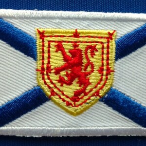 Peut inclure: Un écusson brodé blanc avec une croix diagonale bleue et un écu jaune avec un lion rouge au centre. L'écu est entouré d'une bordure rouge.