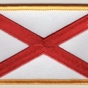 May include: A white patch with a red cross embroidered on it. The patch has a gold border.
