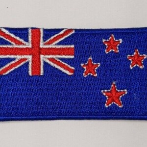 Peut inclure: Un patch brodé représentant le drapeau de la Nouvelle-Zélande. Le drapeau est bleu avec un Union Jack rouge dans le coin supérieur gauche et quatre étoiles rouges à cinq branches dans le coin inférieur droit.