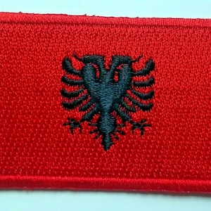May include: A red embroidered patch featuring a black double-headed eagle, the national symbol of Albania.