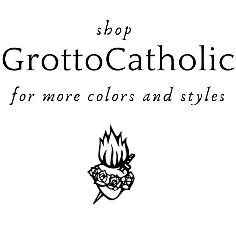 May include: Black and white illustration of a heart with flames on top, surrounded by a wreath of roses and pierced by a sword. The text "shop GrottoCatholic for more colors and styles" is above the image.