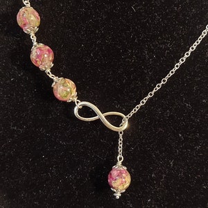 May include: A silver necklace with an infinity charm and four round beads filled with pressed pink and green flowers.