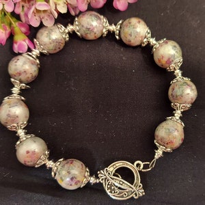 May include: A silver bracelet with a floral pattern on the beads. The bracelet has a toggle clasp.