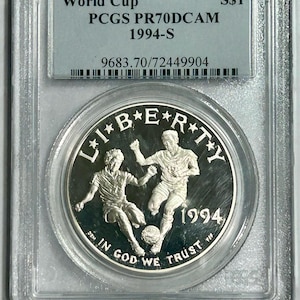 Peut inclure: Une pièce de monnaie en argent dans un boîtier en plastique transparent. La pièce représente deux joueurs de football et les mots "LIBERTY" et "1994". Le boîtier porte l'inscription "World Cup" et "PCGS PR70DCAM 1994-S".