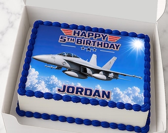 Może przedstawiać: Prostokątne ciasto w białym pudełku z jadalnym obrazkiem szarego odrzutowca lecącego nad chmurami. Tekst głosi HAPPY 5TH BIRTHDAY oraz JORDAN. Ciasto ma niebieskie obwódki z lukru i tło przedstawiające niebieskie niebo ze słońcem.
