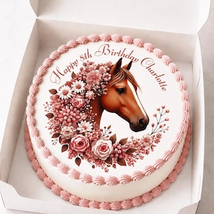 Puede incluir: Un pastel redondo blanco en una caja con una ilustración de una cabeza de caballo marrón rodeada de flores rosas y blancas. El texto "Happy 8th Birthday Charlotte" está impreso en cursiva marrón. Bordes decorados con glaseado rosa.