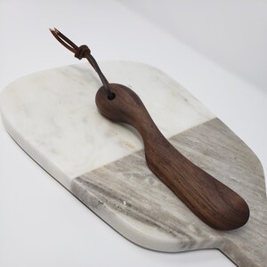 May include: A white and grey marble serving board with a dark brown wooden butter knife with a leather strap.