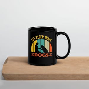 May include: Black ceramic mug with the text "EAT SLEEP WALK DOGS" in a retro design. The design features a silhouette of a person and a dog, with a colorful striped background. A perfect gift for dog lovers.