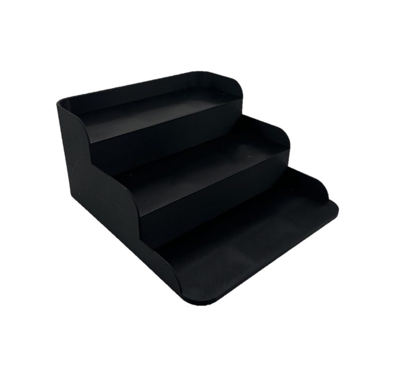 May include: A black three-tiered shelf organizer with a textured base. The shelf is made of plastic and has a modern design.