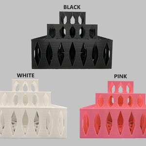 May include: Three tiered display stands in black, white, and pink. Each stand is made of plastic and has a diamond-shaped pattern. The stands are stacked on top of each other.