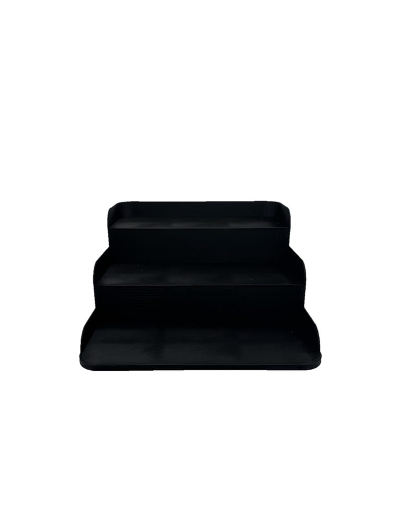 May include: A black three-tiered shelf organizer. The shelf is made of plastic and has a smooth, matte finish.