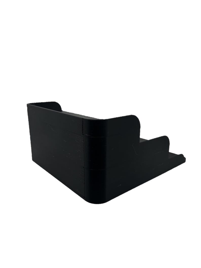 May include: A black plastic tiered storage organizer with three levels. The organizer is designed to hold small items, such as toiletries or office supplies.
