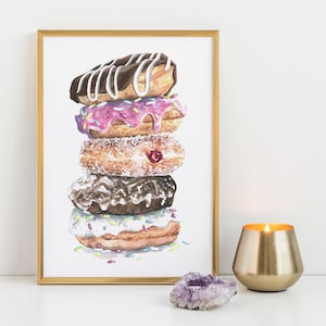 Puede incluir: Impresión de acuarela de una pila de cinco donuts con varios glaseados y chispas. Los donuts están en un marco dorado. Un portavelas dorado con una vela encendida y un cristal púrpura están en primer plano.