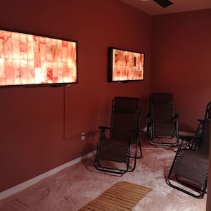 May include: A salt therapy room with a pink Himalayan salt floor, four black reclining chairs, and three salt lamps on the walls.
