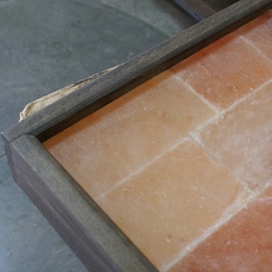 May include: A wooden frame with a salt tile insert. The tiles are a light pink color and are arranged in a grid pattern.