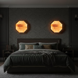 May include: A bedroom scene featuring a bed with a dark green comforter and pillows. Two octagonal, illuminated wall sconces with a warm, amber glow flank the bed. The room has dark walls, a rug, and a wooden headboard.
