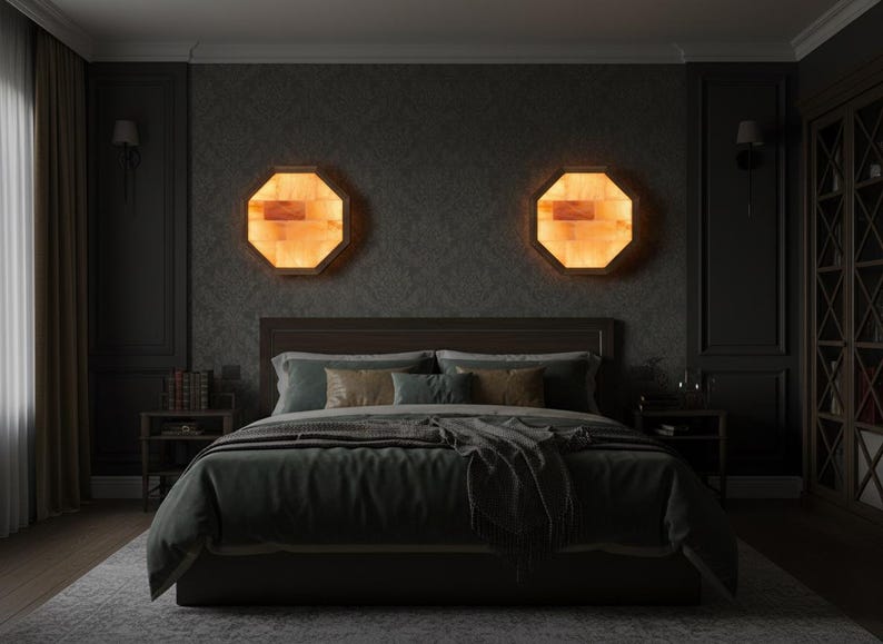 May include: A bedroom scene featuring a bed with a dark green comforter and pillows. Two octagonal, illuminated wall sconces with a warm, amber glow flank the bed. The room has dark walls, a rug, and a wooden headboard.