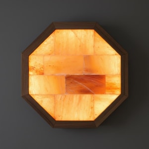 May include: An octagonal wall-mounted Himalayan salt lamp. The lamp features a wooden frame and is filled with illuminated orange salt crystals. The lamp is a decorative and functional item, providing a warm, ambient glow.