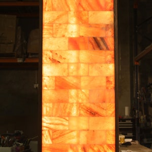 May include: A rectangular salt lamp made of Himalayan salt bricks, with a warm orange glow emanating from within the lamp. The lamp is framed in a dark wood frame.