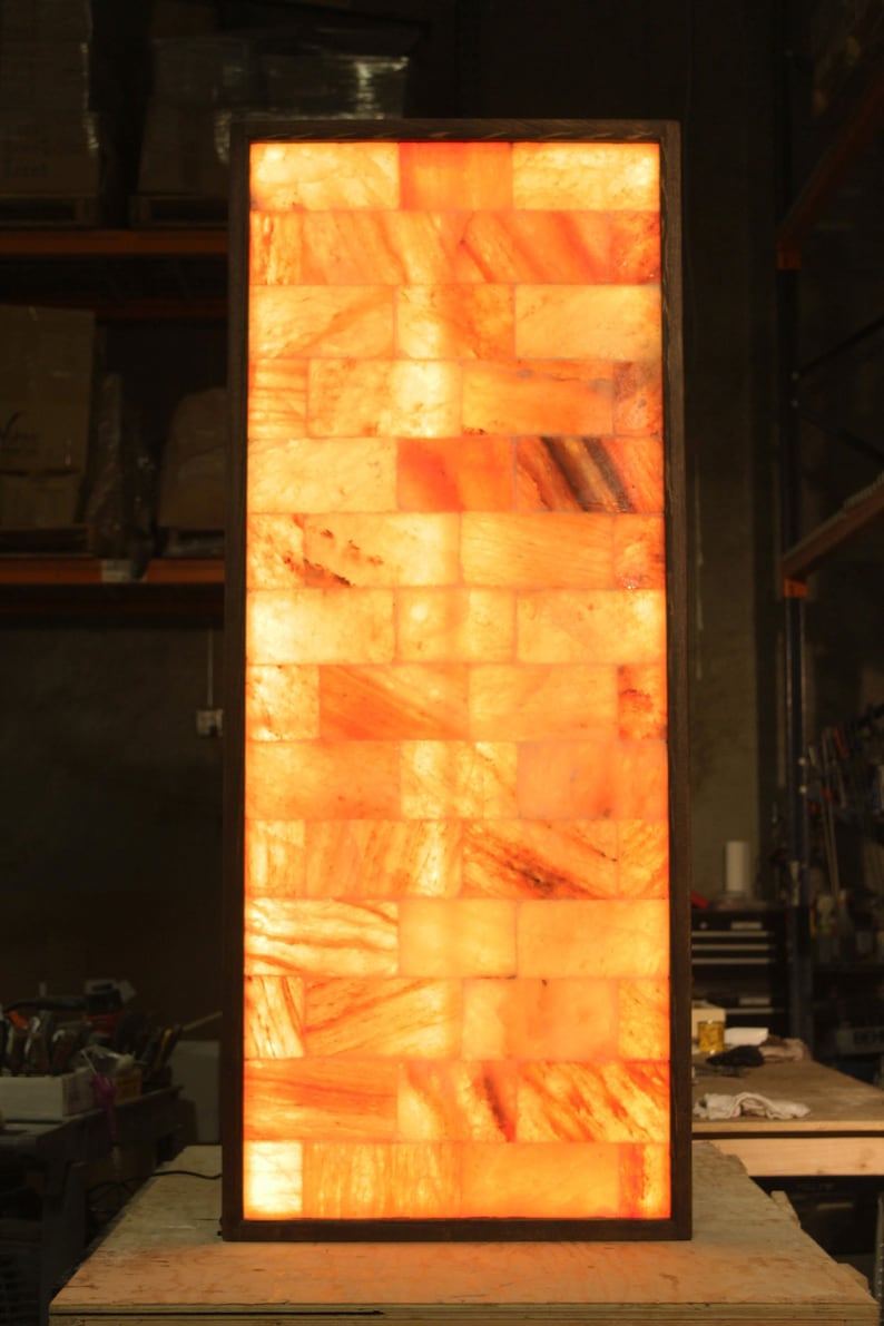 May include: A rectangular salt lamp made of Himalayan salt bricks, with a warm orange glow emanating from within the lamp. The lamp is framed in a dark wood frame.