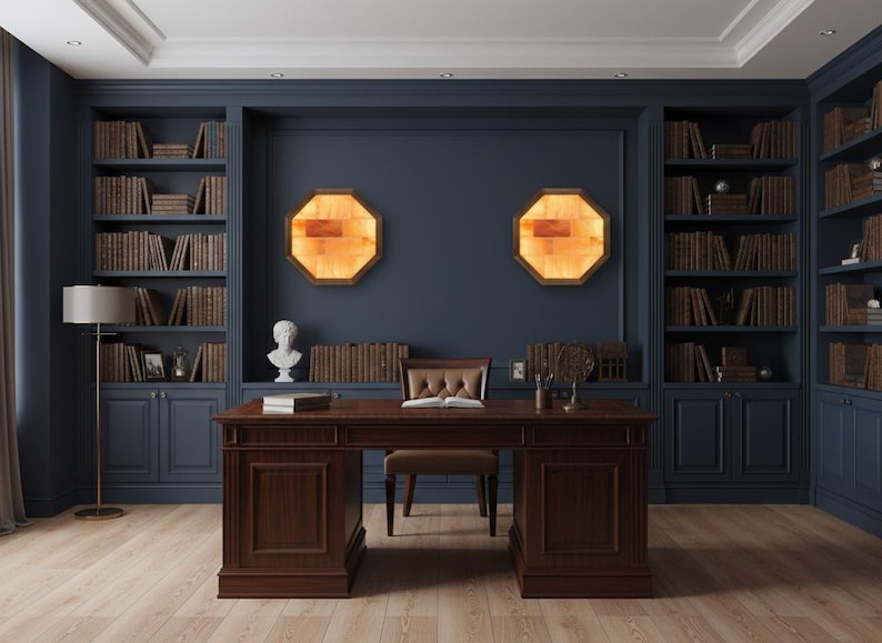 May include: A home office with dark blue walls and built-in bookshelves filled with books. A large wooden desk with a leather chair sits in front of the wall. Two octagonal, illuminated wall sconces and a bust sculpture add to the room's decor.