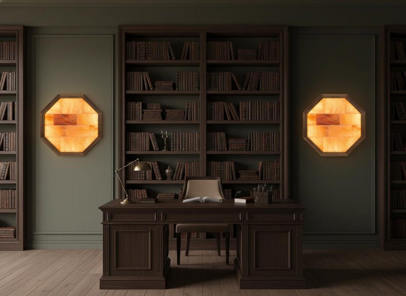 May include: A dark wood desk with a matching chair sits in front of a large bookshelf filled with books. Two octagonal wall sconces with a warm orange glow flank the bookshelf. A brass desk lamp is on the desk.