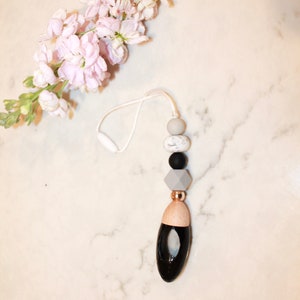 May include: A black and white car air freshener with a wooden top and a beaded string. The beads are grey, white, and black.