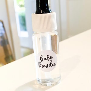 May include: A clear glass bottle with a white cap and a black dropper. The bottle has a white label with the text "Baby Powder" in black lettering. The bottle is labelled as a diffuser refill.