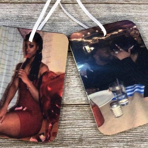 Pode incluir: Dois aromatizadores de carro com foto e cordas brancas. O primeiro aromatizador apresenta uma mulher com um vestido vermelho segurando um balão vermelho em forma de coração. O segundo aromatizador apresenta um casal se abraçando em uma mesa de restaurante.