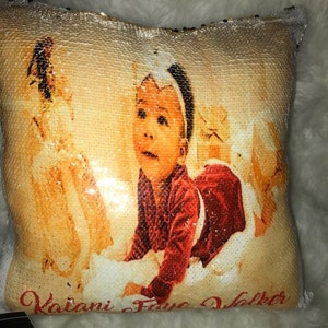 May include: A gold sequin pillow with a photo of a baby girl printed on it. The pillow has the text "Kaiani Faye Walker" printed on the bottom.