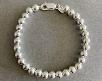 May include: A silver beaded bracelet with a clasp closure. The beads are round and smooth.